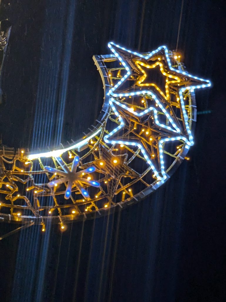 A close up photograph of one of the Christmas lights. It shows an illuminated shooting star against the night sky.